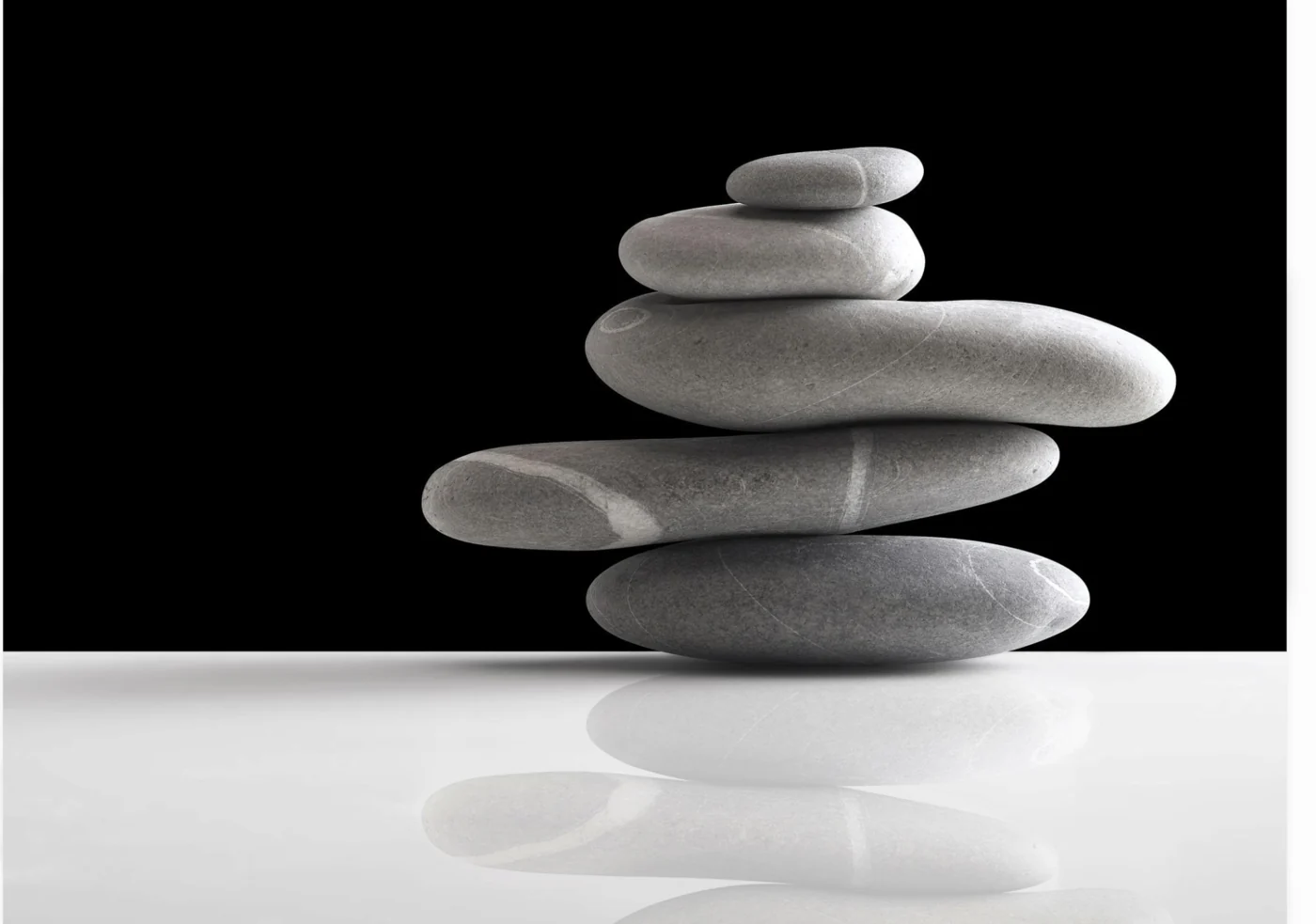 Piedras grises de distintas formas que se sostienen en equilibrio, sobre una superficie con reflejo.
